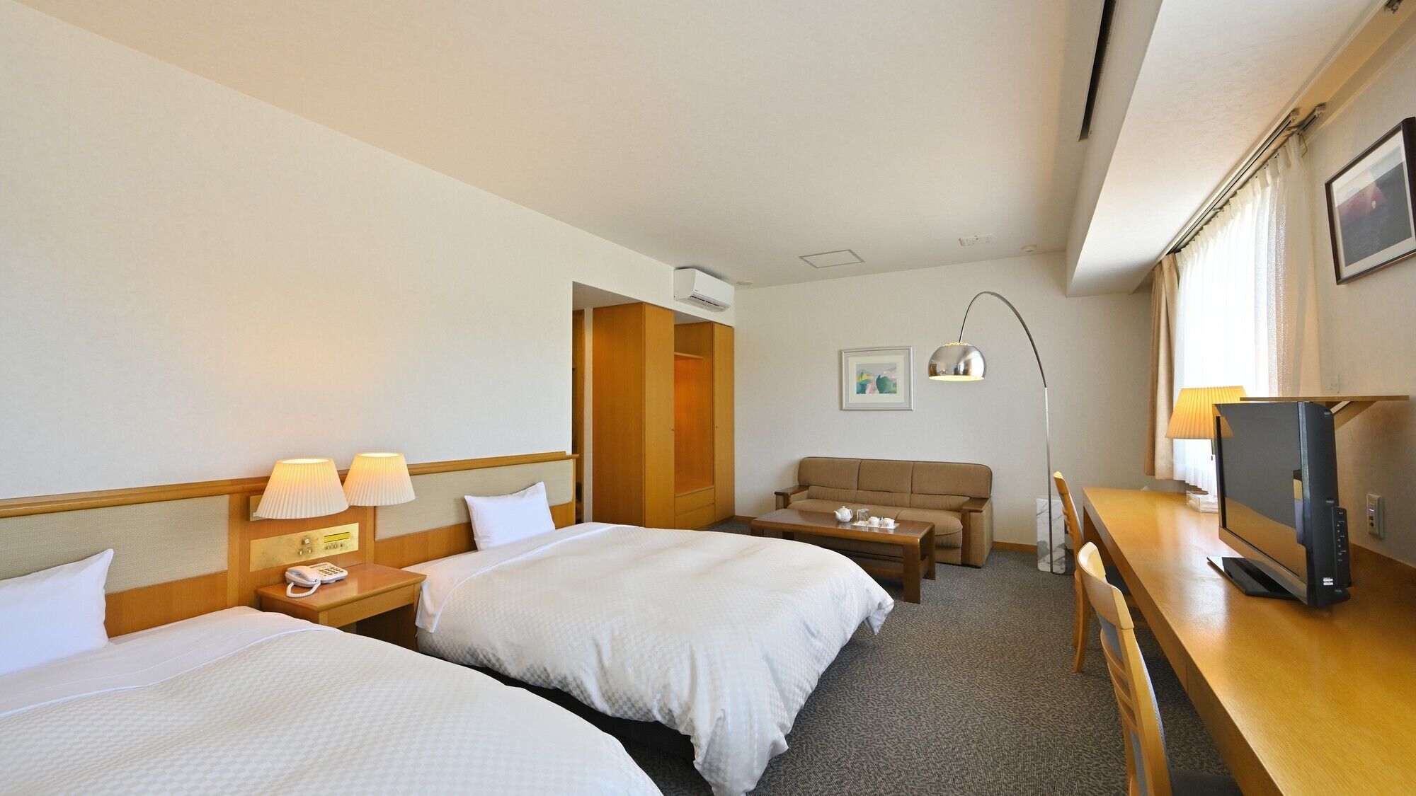 Habitación de hotel con dos camas, un sofá, un escritorio con televisor y una lámpara.