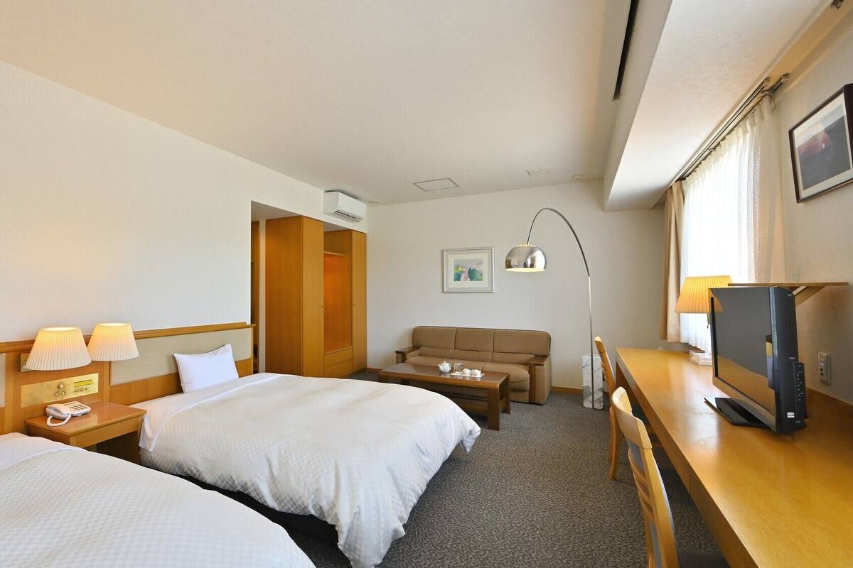 Une chambre d’hôtel avec deux lits, un canapé, un bureau avec une télévision et une lampe.
