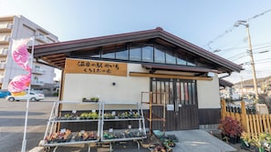 Ein Gebäude mit einem Schild in japanischer Schrift, ein Laden mit Topfpflanzen und ein Holzzaun im Hintergrund.