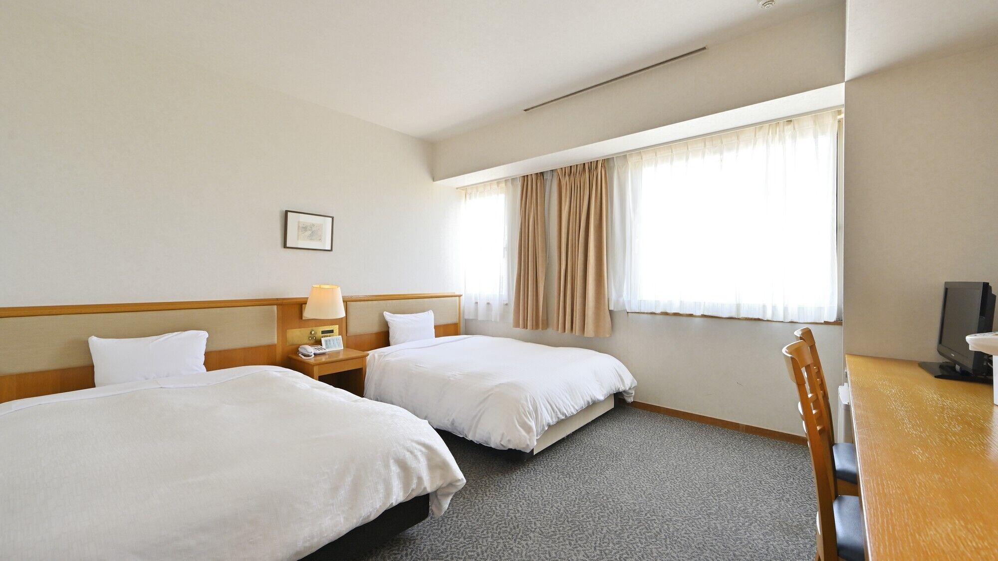 Habitación de hotel con dos camas, un escritorio, una silla, un televisor y una ventana con cortinas.