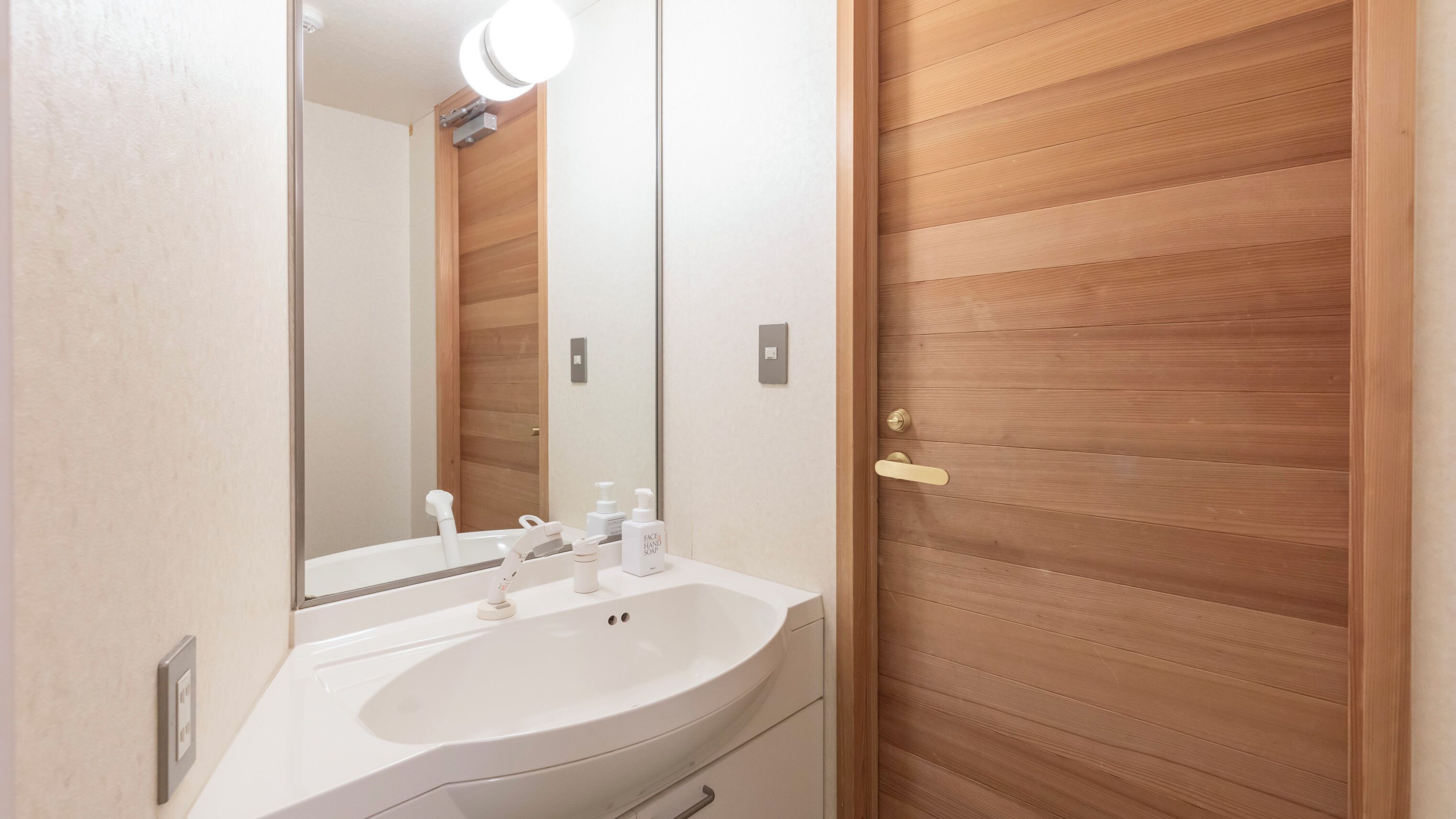 Un baño con lavamanos blanco, un espejo y una puerta de madera.