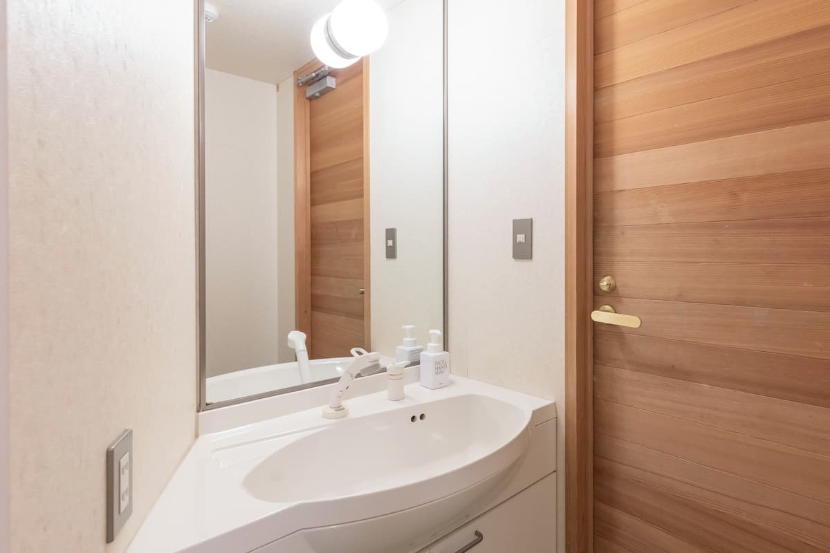 Une salle de bain avec un lavabo blanc, un miroir et une porte en bois.
