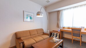 Une pièce comprenant un canapé, une table, une lampe, une chaise, un bureau, une fenêtre avec des rideaux et un tableau encadré accroché au mur.