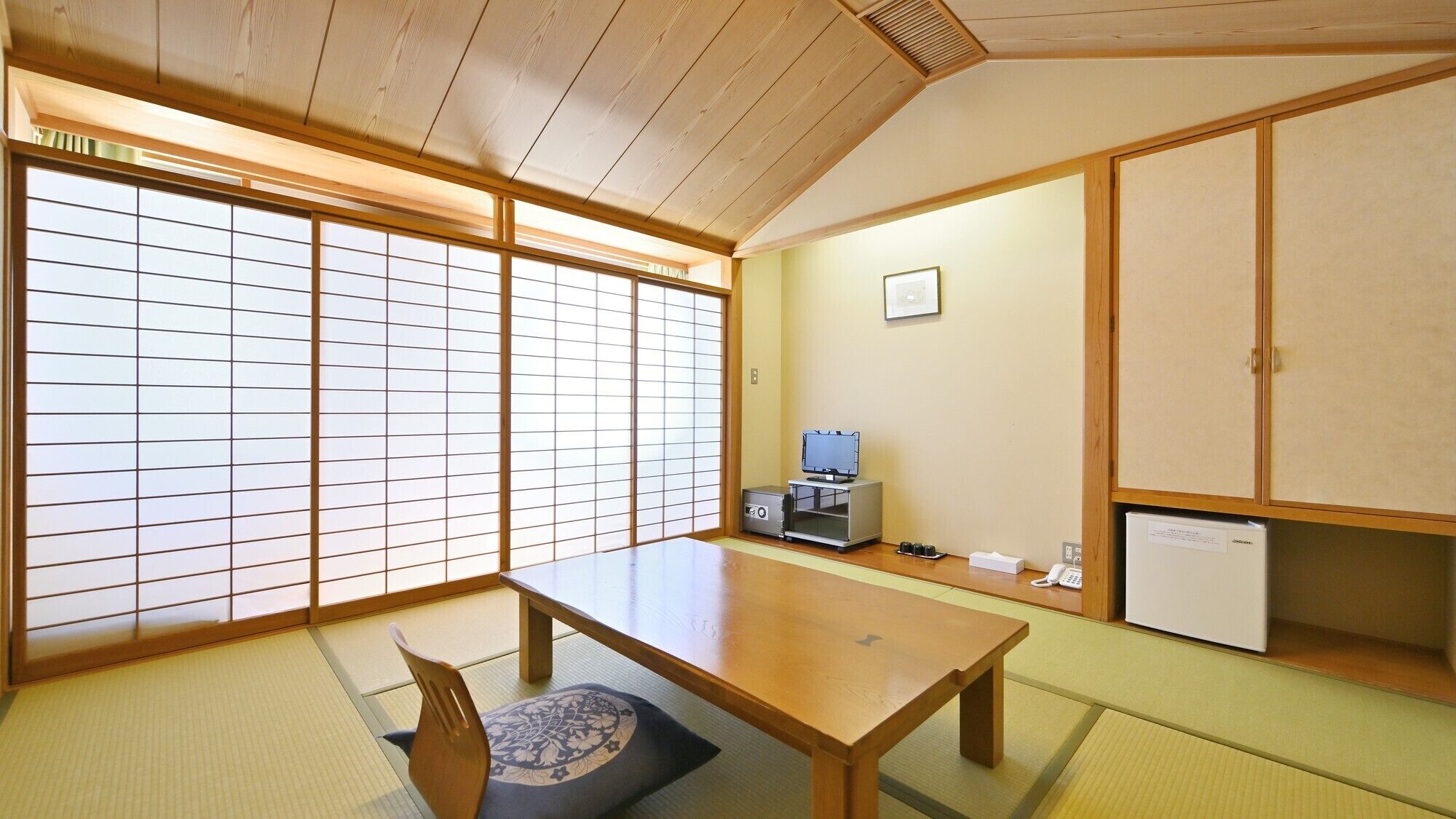 Una habitación japonesa tradicional con suelo de tatami, una mesa baja, un televisor y un armario.