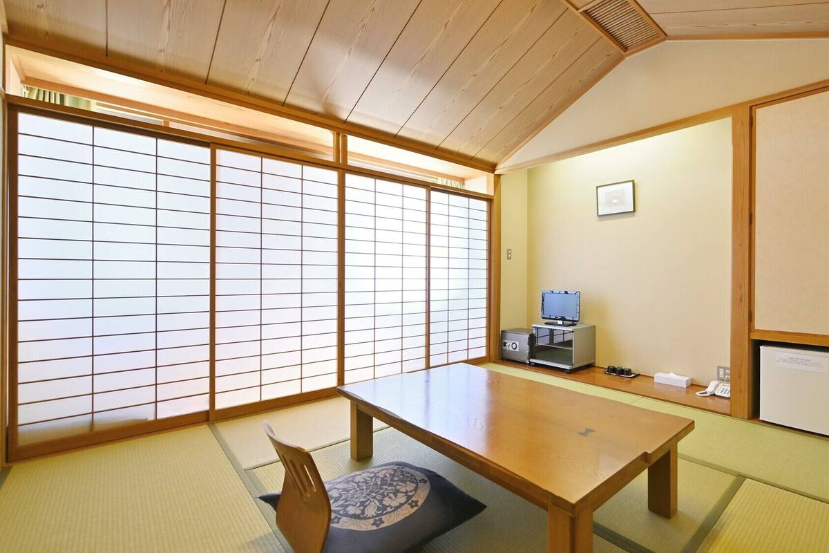 Une pièce de style japonais traditionnel, avec un sol recouvert de tatamis, une table basse, un téléviseur et un meuble.