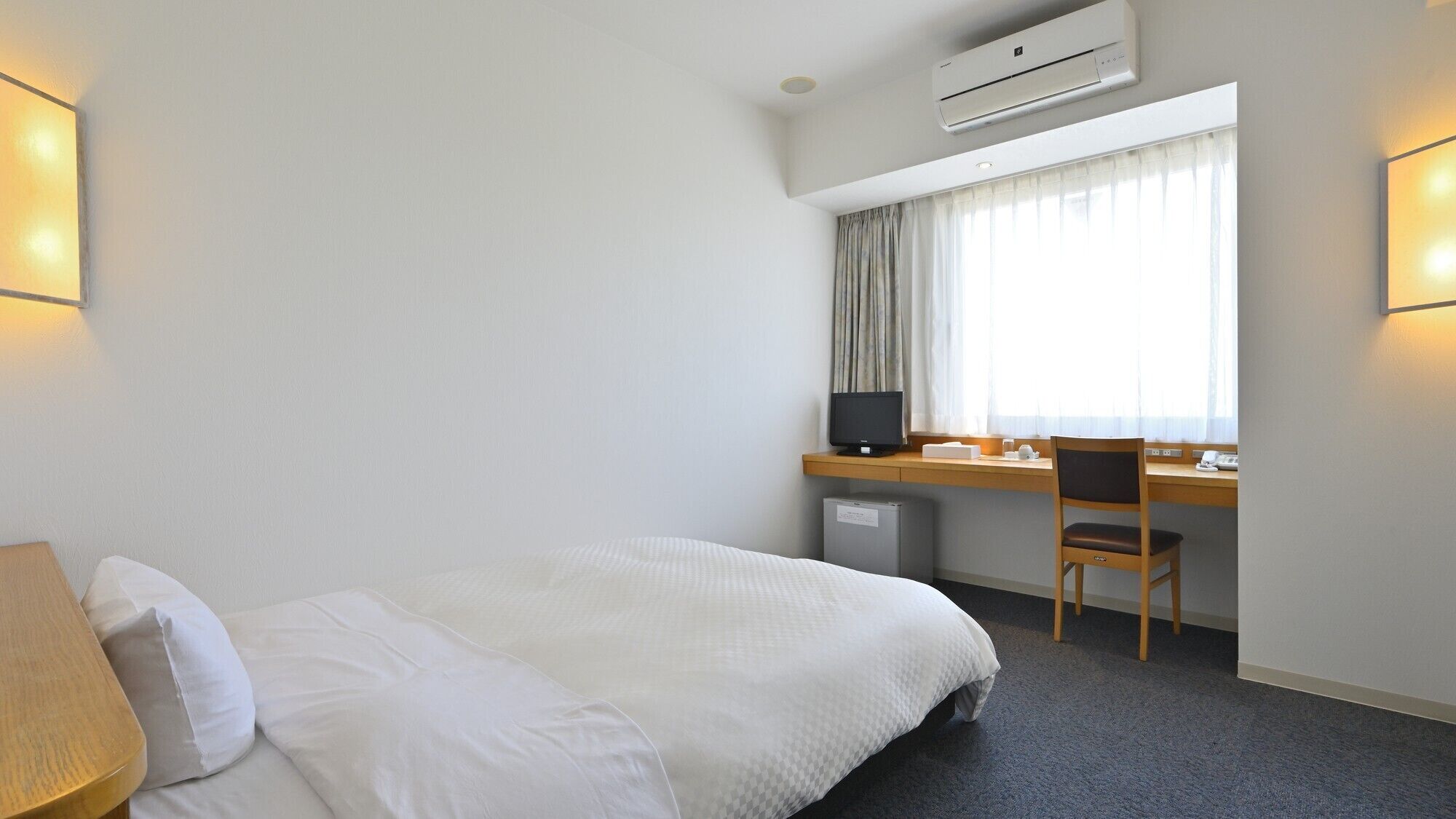 Una habitación de hotel con cama, escritorio, silla y aire acondicionado.
