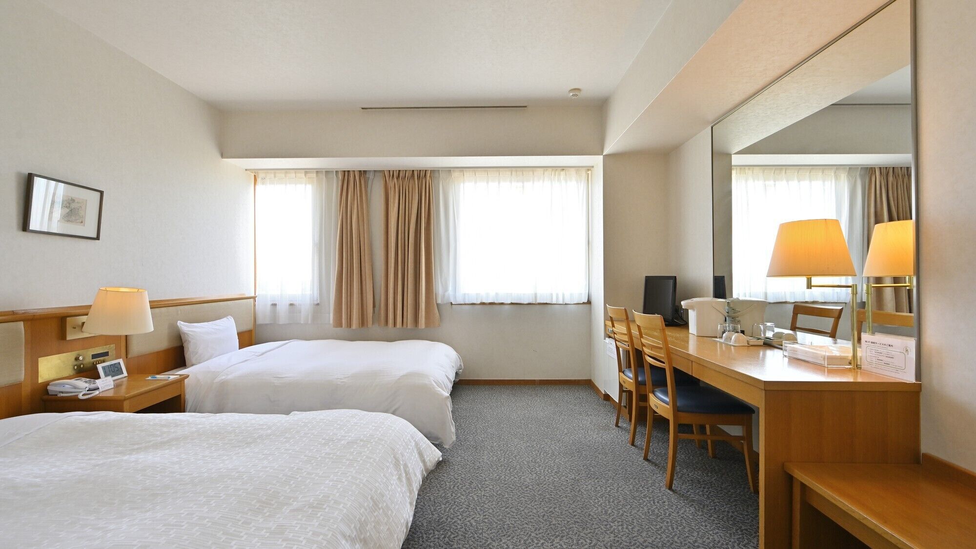 Habitación de hotel con dos camas, un escritorio, una silla, un espejo, una lámpara y un reloj.