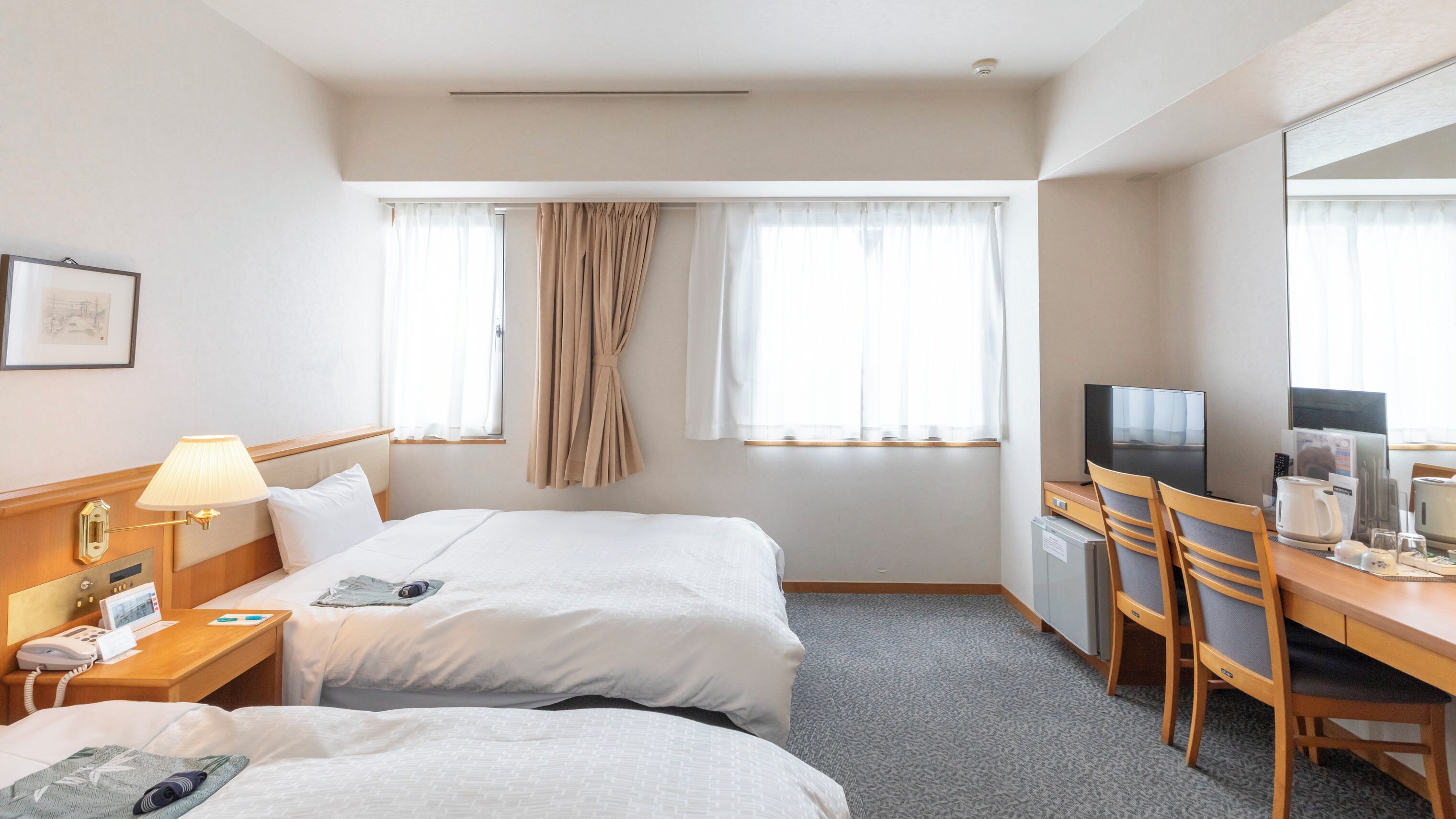 Habitación de hotel con dos camas, un escritorio con televisor, cafetera y refrigerador pequeño.