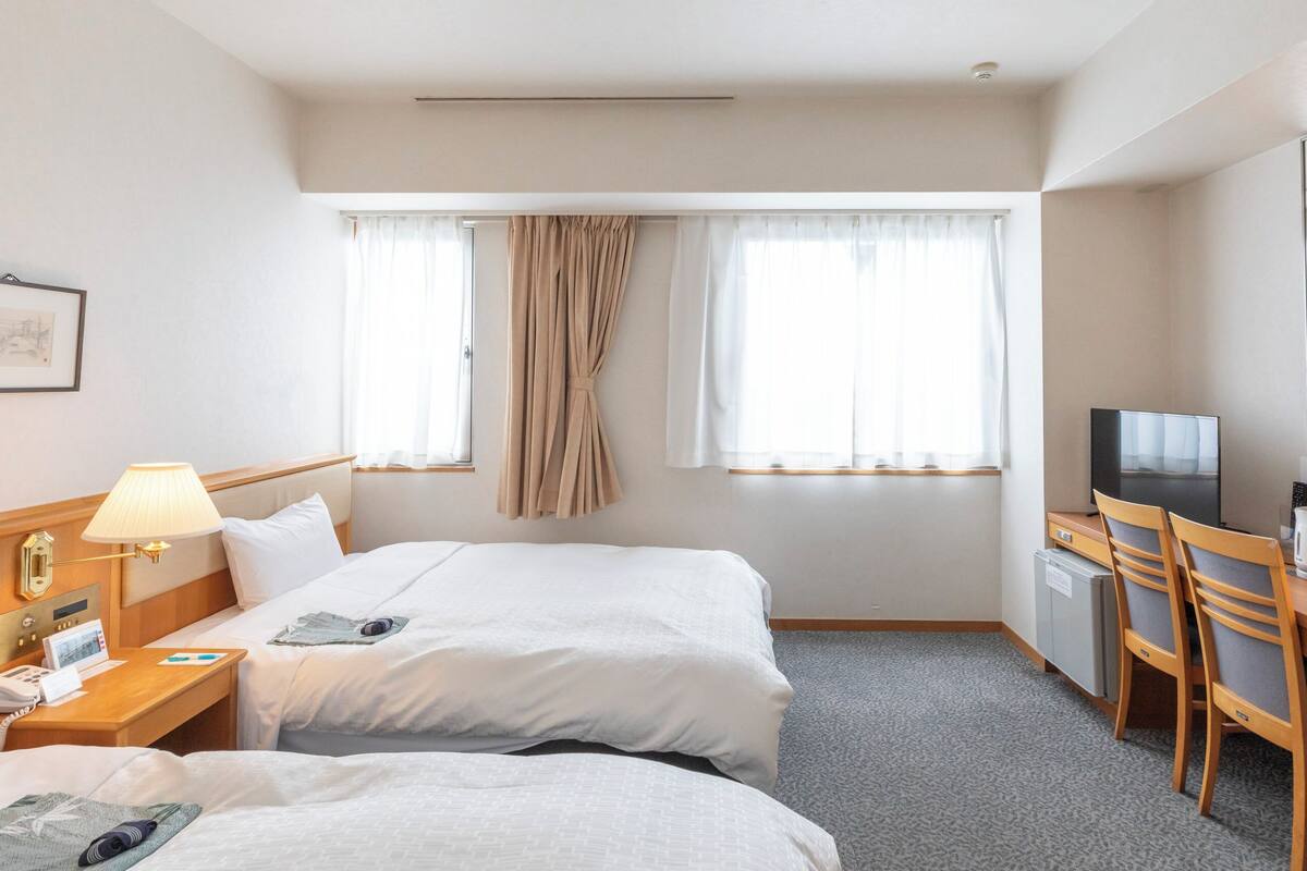 Une chambre d’hôtel avec deux lits, un bureau avec une télévision, une machine à café et un petit réfrigérateur.