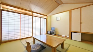 A traditional Japanese room with tatami flooring, a low wooden table, a television, and a refrigerator.
