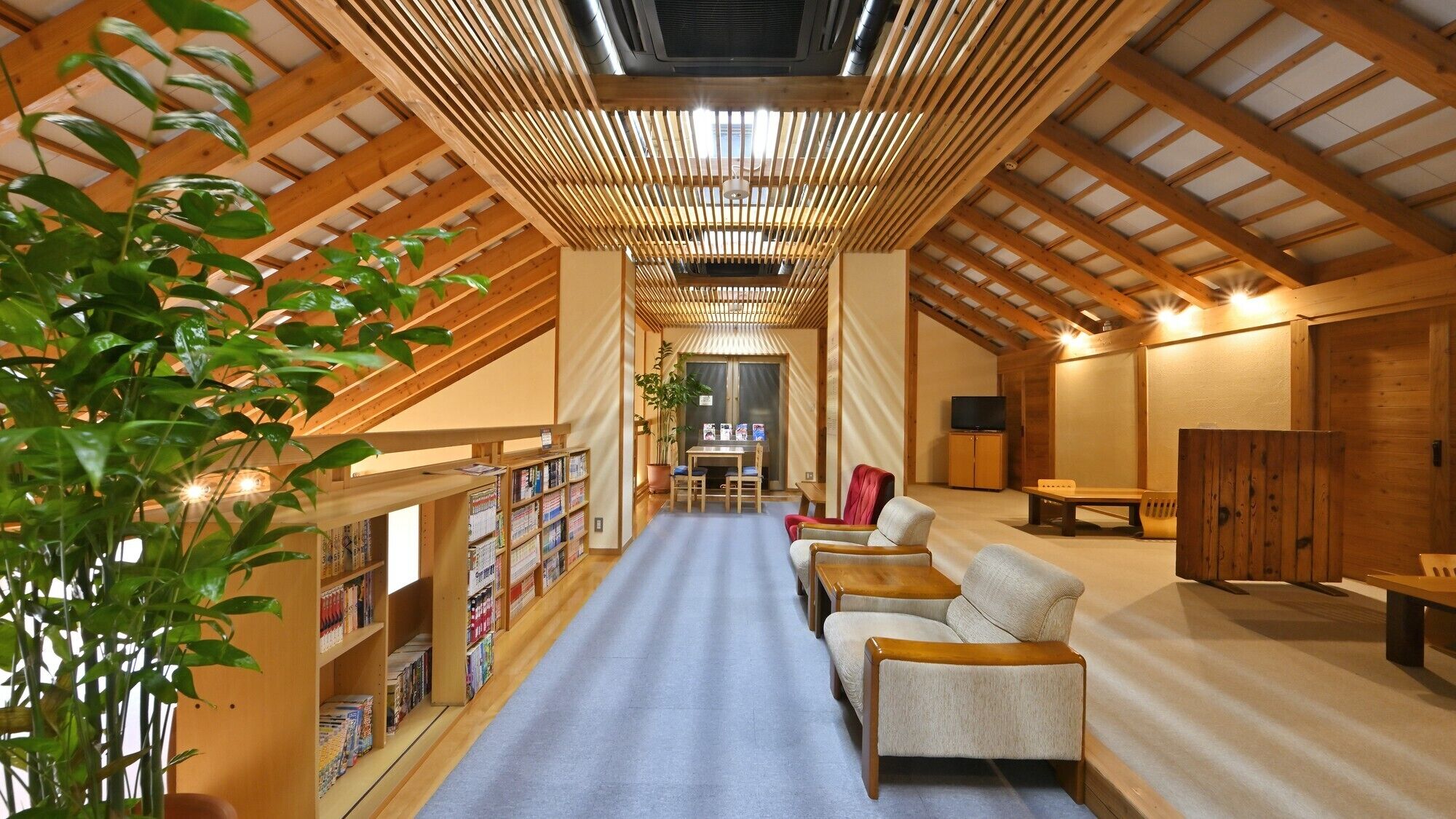 A spacious loft with a high ceiling, wooden beams, a central seating area, and a bookshelf.