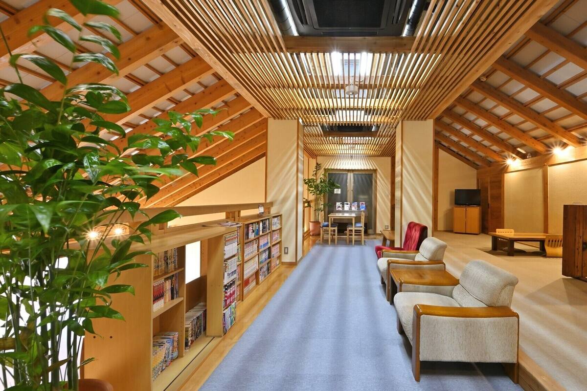 Un loft spacieux avec un plafond haut, des poutres apparentes, un coin salon central et une bibliothèque.