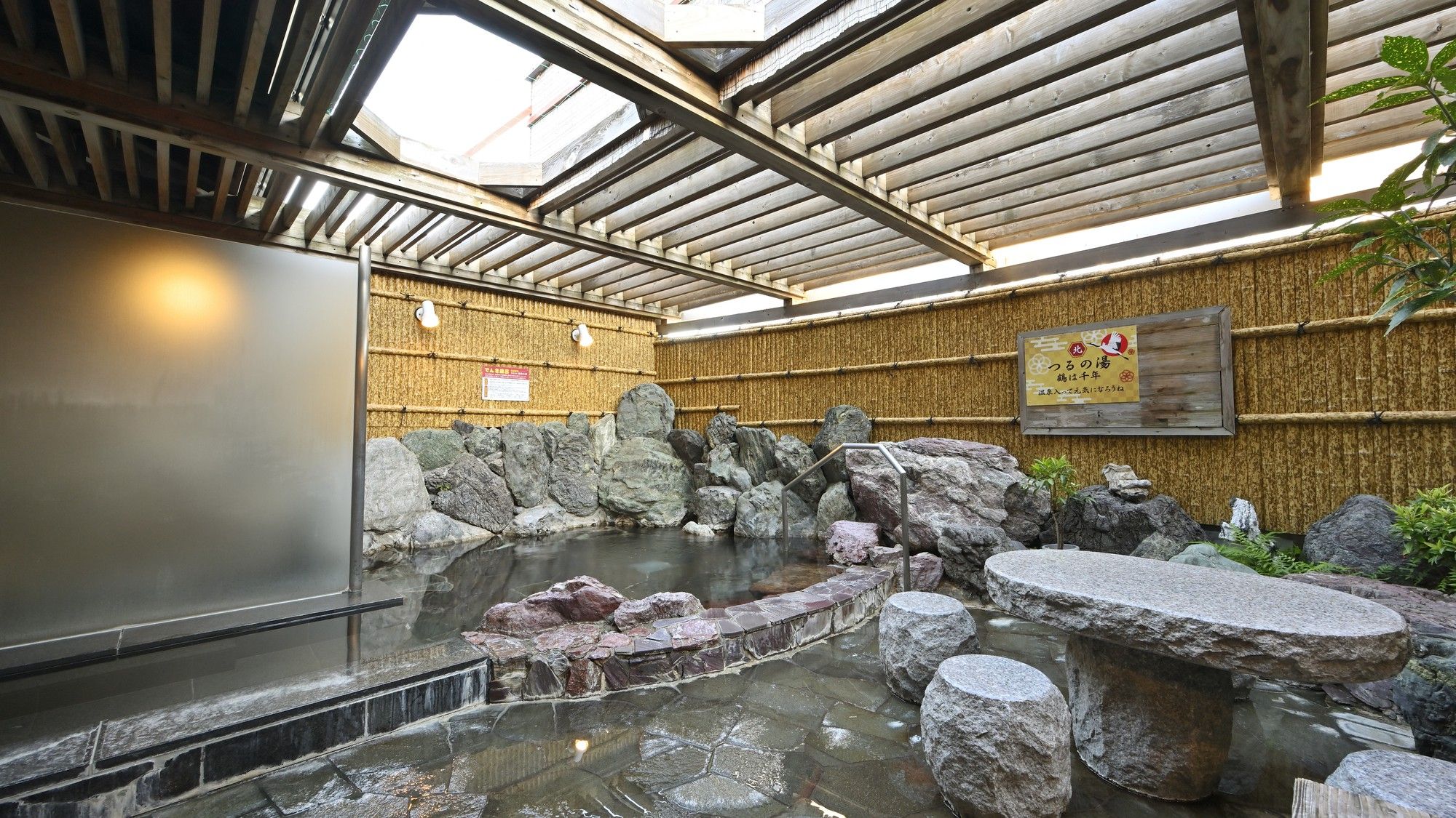 A traditional Japanese onsen with a stone bath surrounded by rocks, a wooden wall, and a bamboo fence.