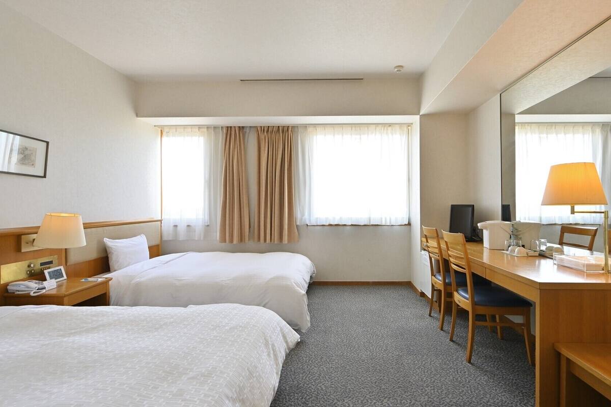 Une chambre d’hôtel avec deux lits, un bureau avec une chaise, une lampe de bureau, un téléphone et un miroir.