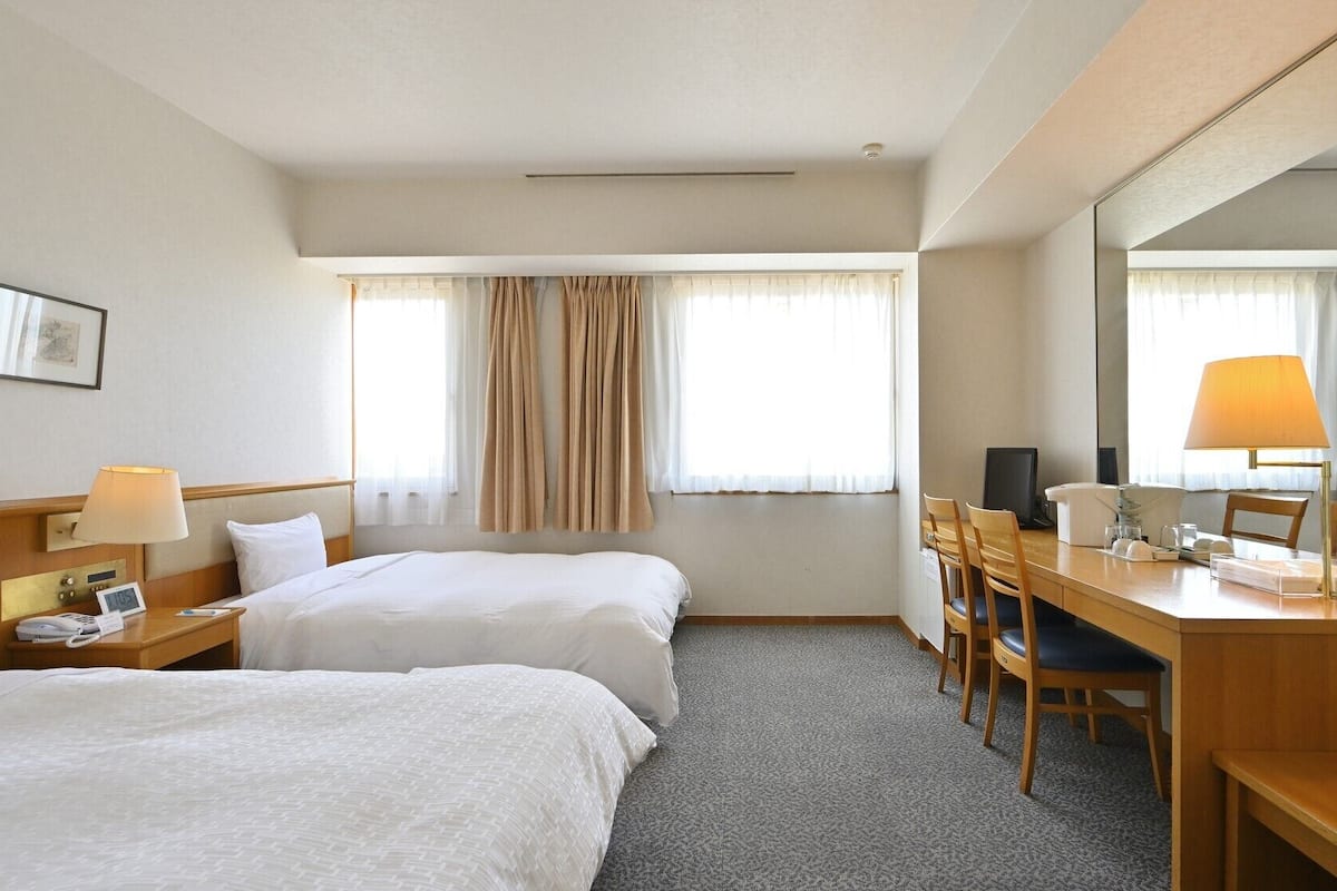 A hotel room with two beds, a desk with a chair, a desk lamp, a telephone, and a mirror.