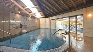 An indoor swimming pool with tiled walls, a wooden ceiling, and a glass door leading outside. - Kochi Kuroshio Hotel (Konan)