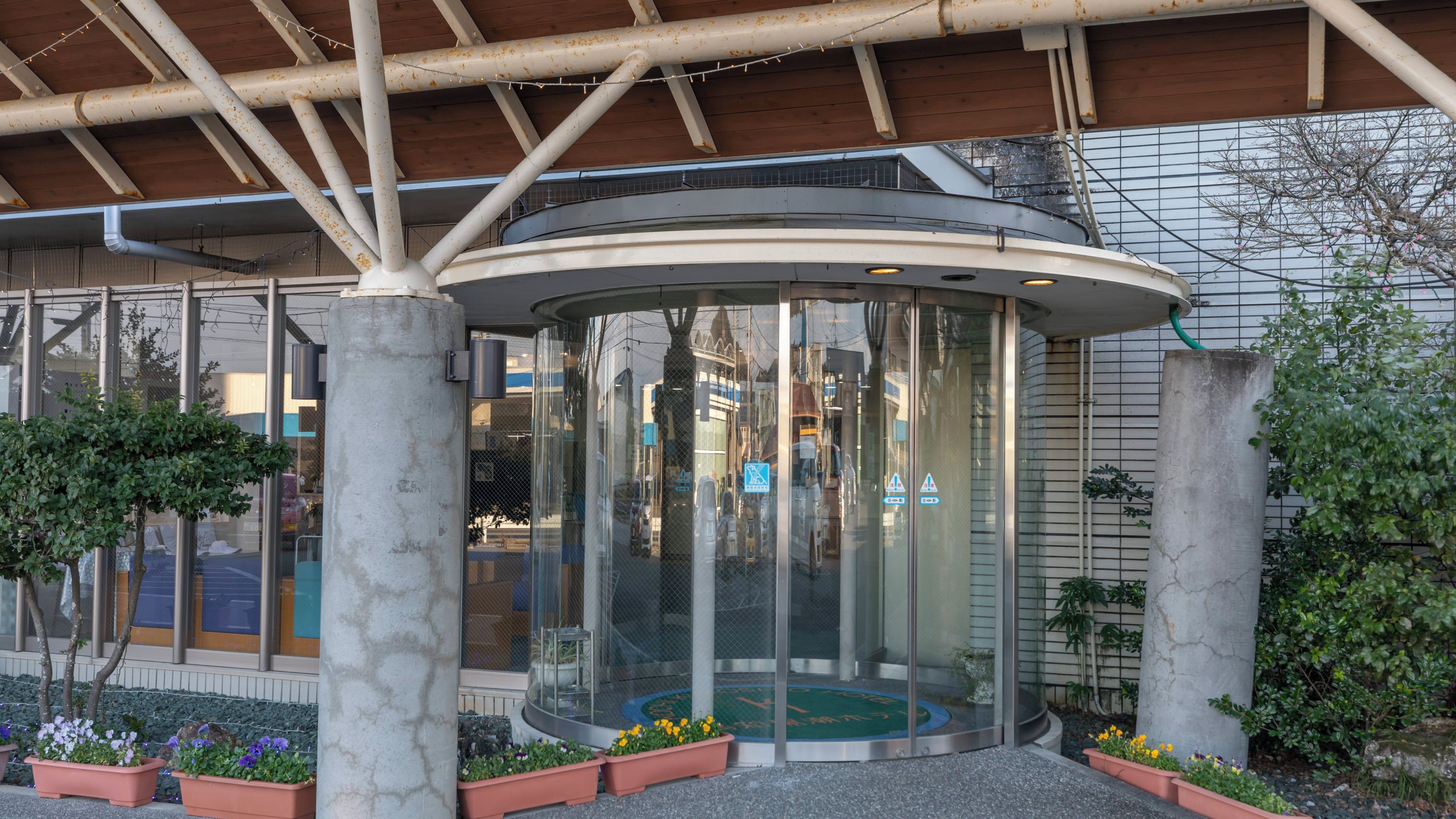 A modern building with a glass elevator, surrounded by potted plants and a metal structure.