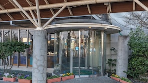 A modern building with a glass elevator, surrounded by potted plants and a metal structure. - Kochi Kuroshio Hotel (Konan)