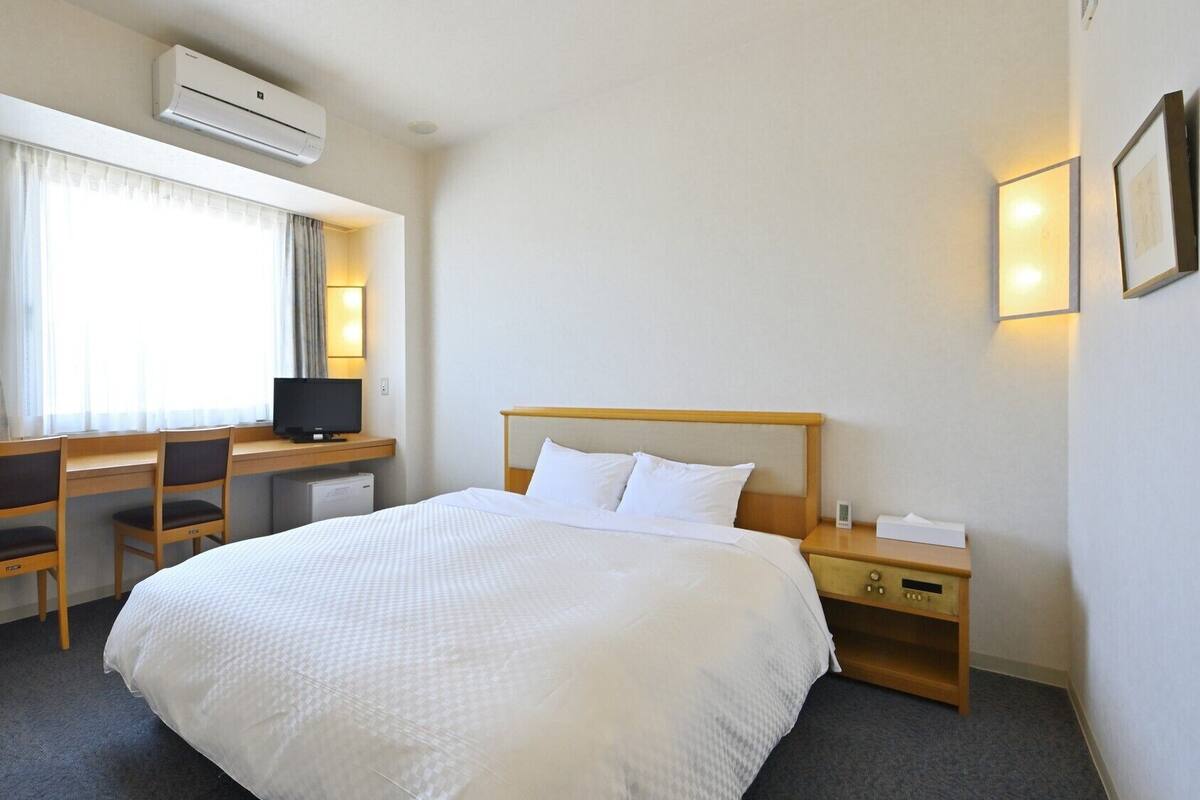 Une chambre d’hôtel équipée d’un lit, d’un bureau, d’une chaise, d’une télévision et d’une table de chevet.