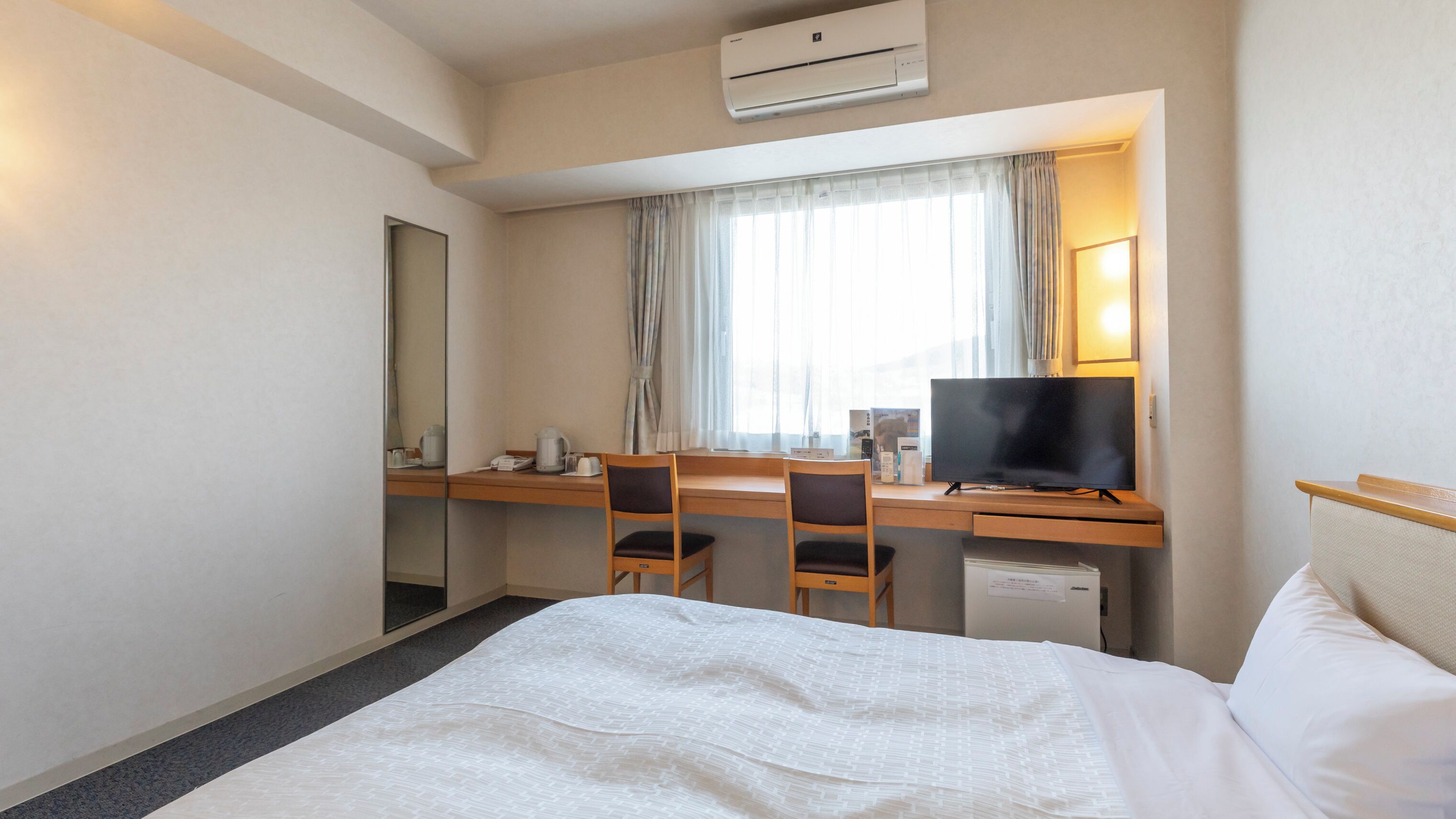 Una habitación de hotel con cama, escritorio, computadora, televisor y espejo.