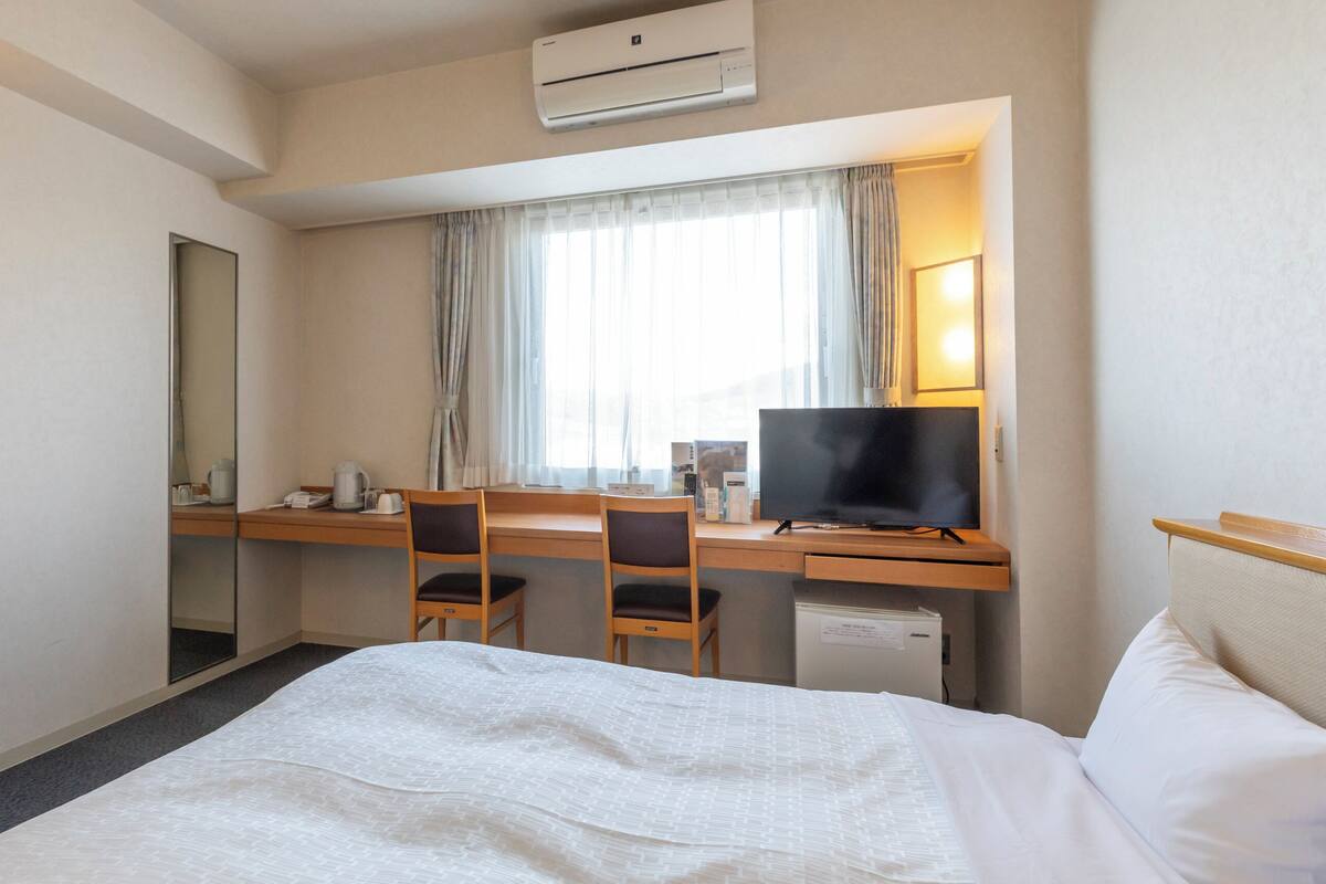 Une chambre d’hôtel avec un lit, un bureau avec un ordinateur, une télévision et un miroir.