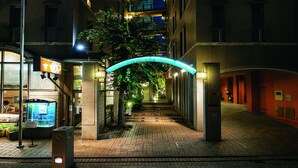 A nighttime urban street with modern buildings, a pedestrian walkway, and a neon-lit archway. - Hotel Patio Dogo (Matsuyama)