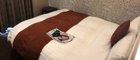 A neatly made bed with a brown blanket and pillows, a striped pillowcase, and a small bedside table with a chair.