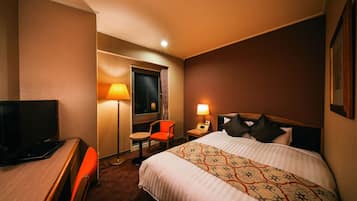 Une chambre d’hôtel comprenant un lit, un bureau avec une télévision, une chaise, une lampe et une table de chevet.