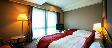 A hotel room with two beds, a desk, a chair, and a TV.