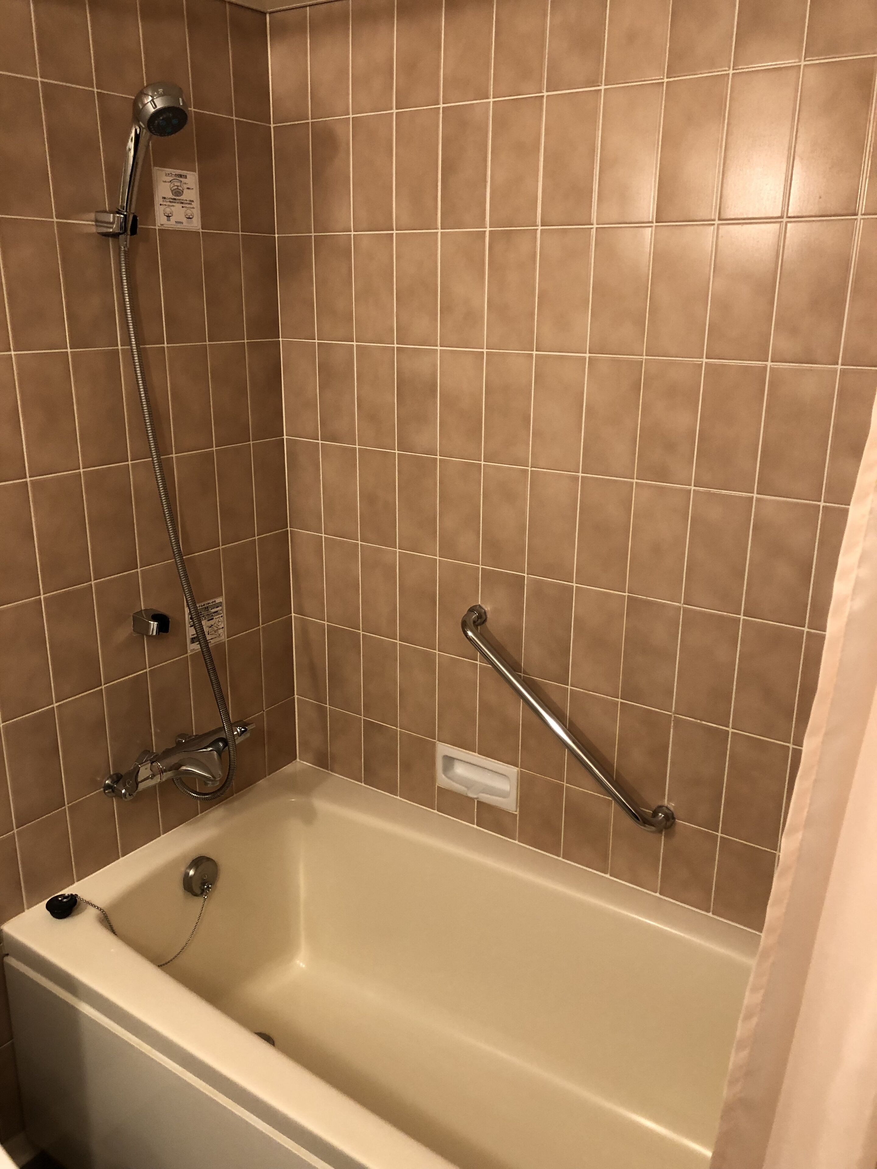 A bathroom with a bathtub, a handheld showerhead, and a grab bar.