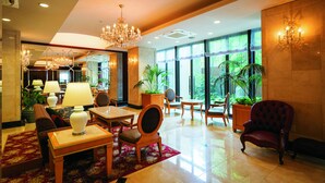 A spacious lobby with a chandelier, comfortable seating, and large windows offering a view of greenery outside. - Hotel Patio Dogo (Matsuyama)