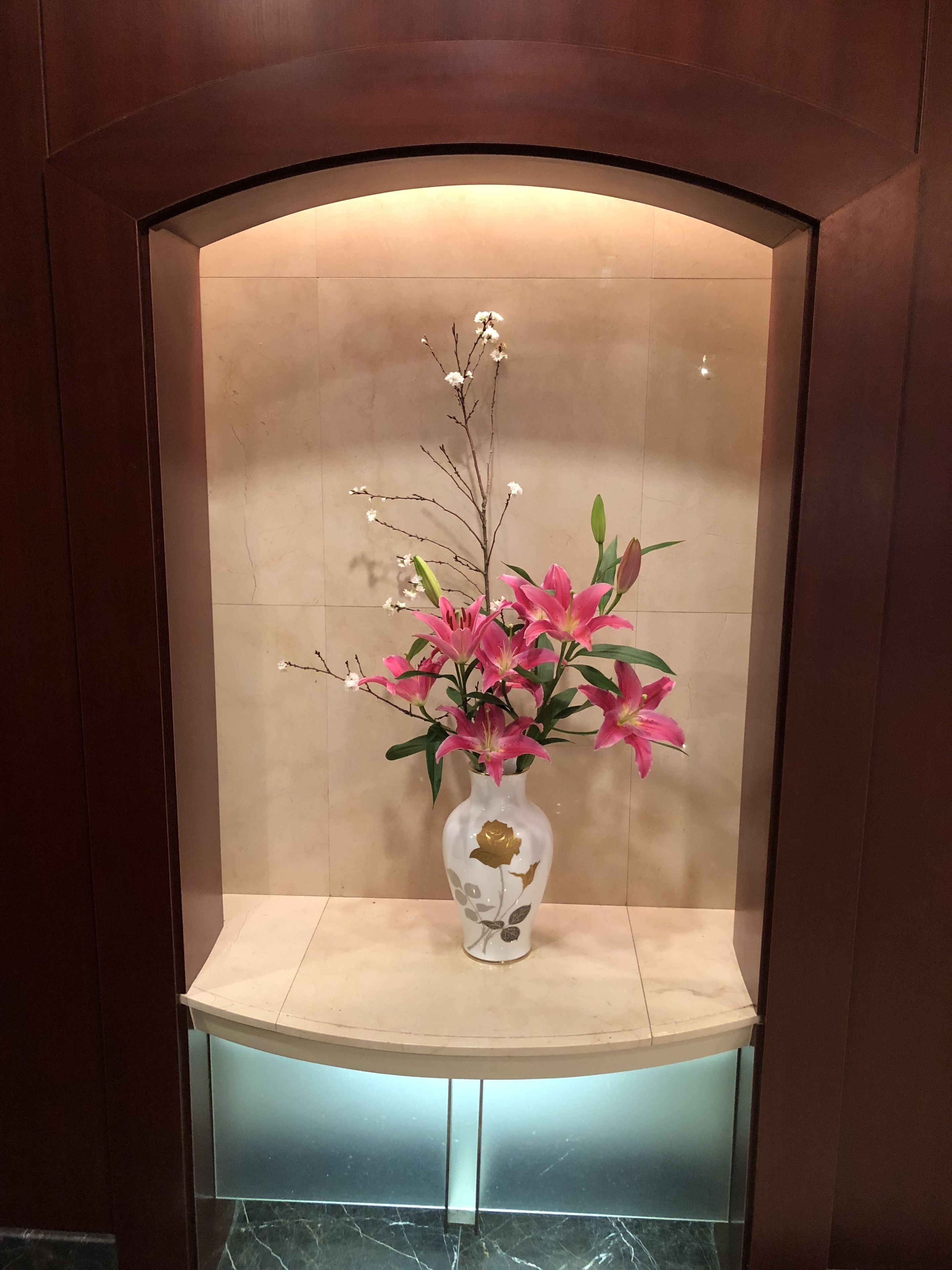 Un jarrón con flores rosadas y una rama con capullos blancos en un nicho empotrado.