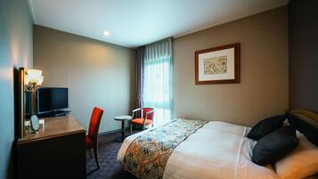 A hotel room with a bed, a desk with a television, a chair, and a small table.