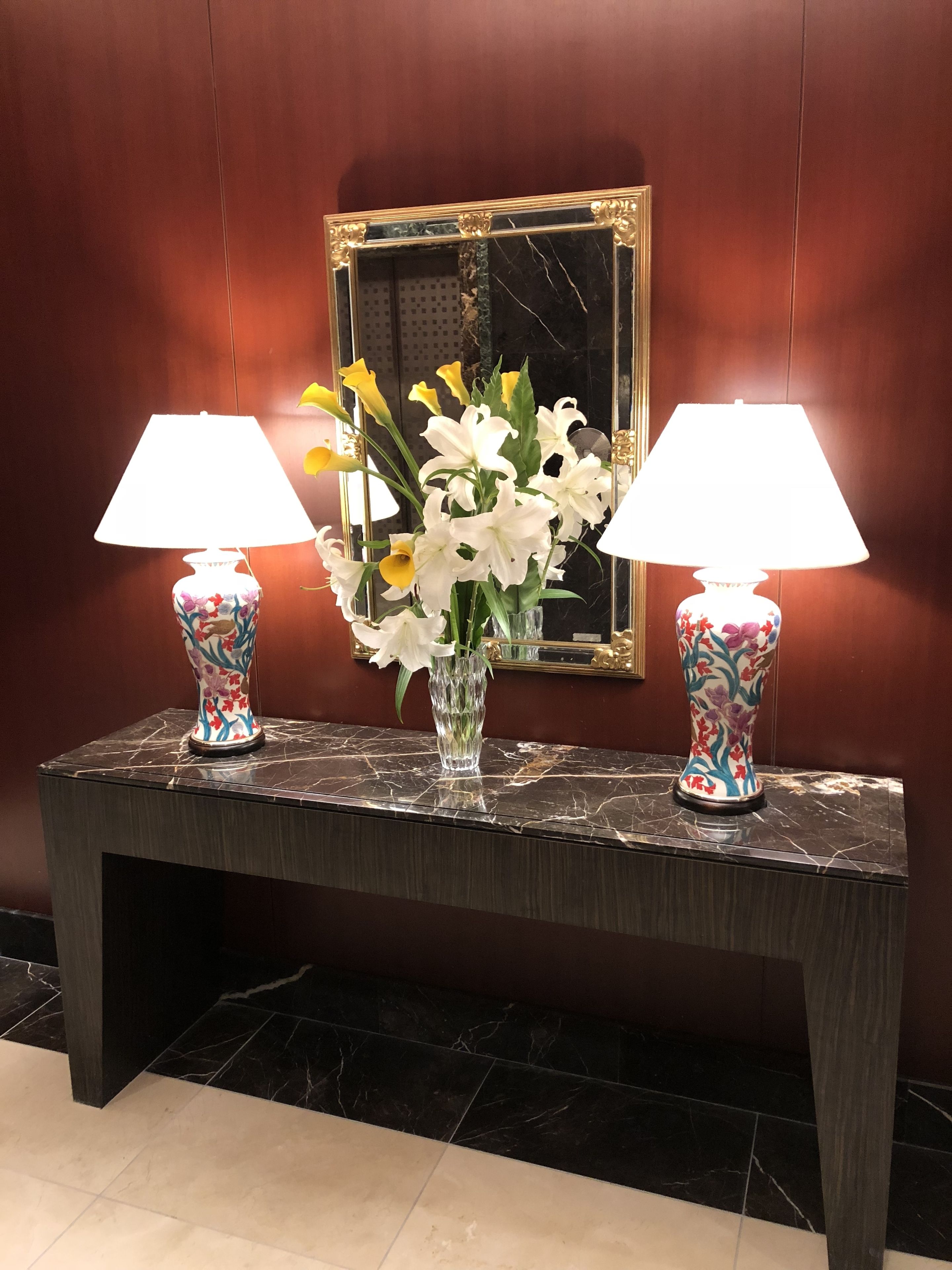 Un comptoir d’accueil en marbre, agrémenté de deux lampes et d’un vase de fleurs.