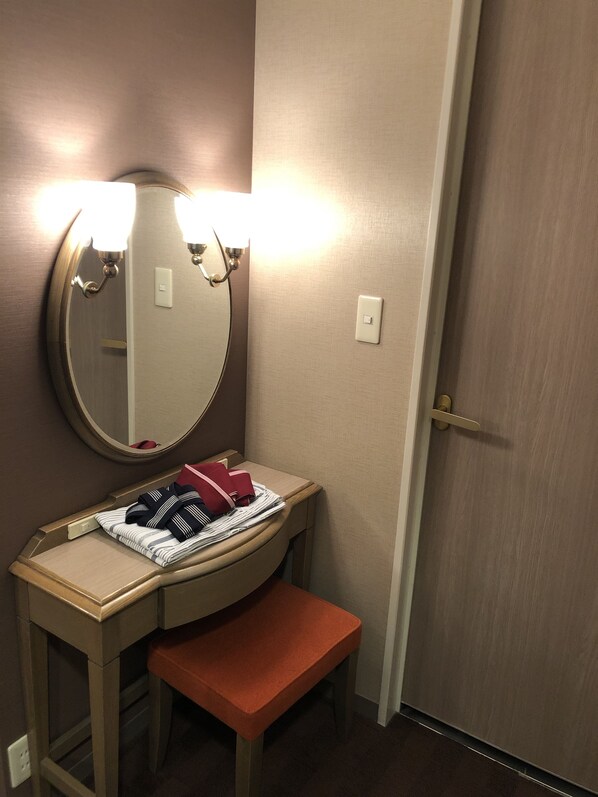 Un tocador de baño con un espejo redondo, dos luces empotradas, una toalla y un banco.