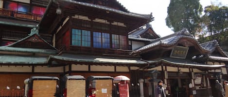 A traditional Japanese building with a tiled roof and wooden structure. There are several large, covered wooden boxes in front of the building.