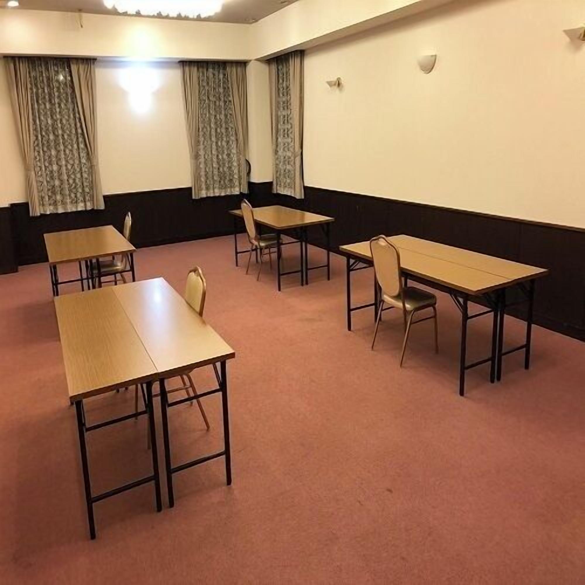 A conference room with four tables and chairs, a carpeted floor, and curtains on the windows.