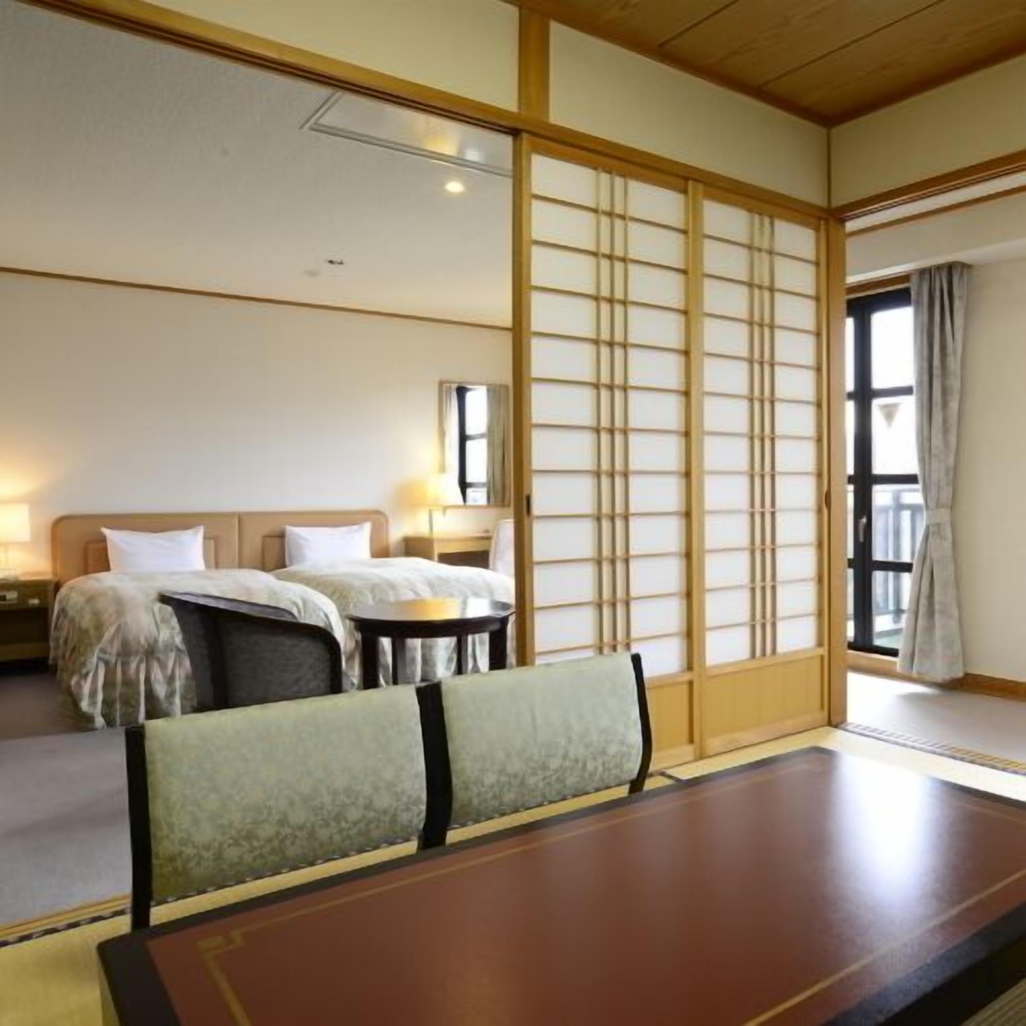 A traditional Japanese-style room with tatami flooring, a low wooden bed, a small table, and a sliding shoji screen.