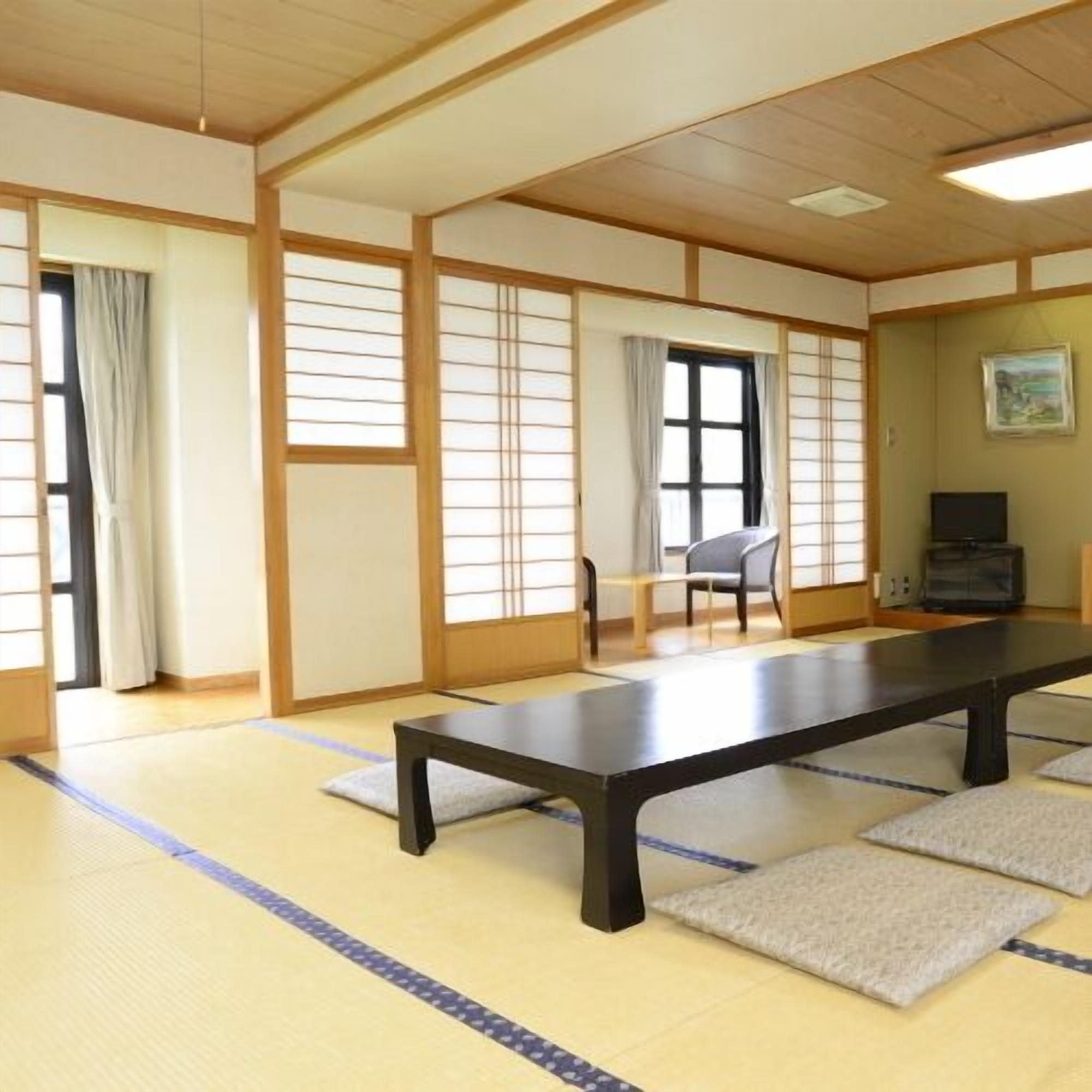 Una habitación japonesa tradicional con suelo de tatami, una mesa baja, una silla y un televisor.