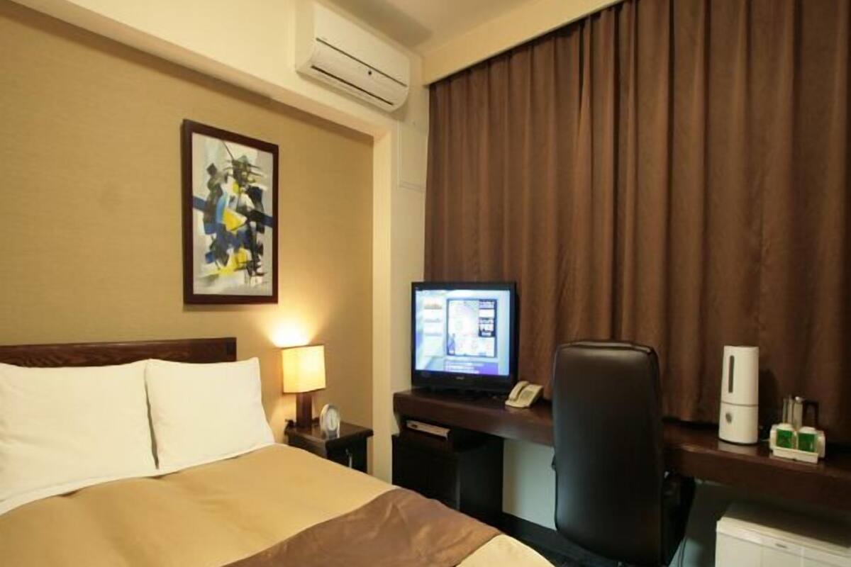 Ein Hotelzimmer mit Bett, Schreibtisch, Computer und einem Fenster mit Vorhängen.