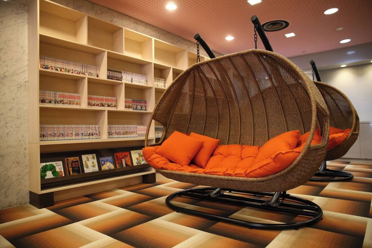 A room with a wicker chair with orange cushions, a bookshelf with books, and a patterned floor.