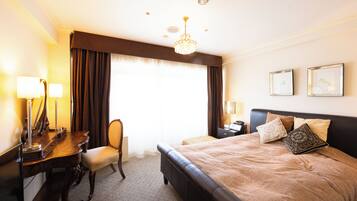 A hotel room with a bed, desk, chair, and a large window with curtains.