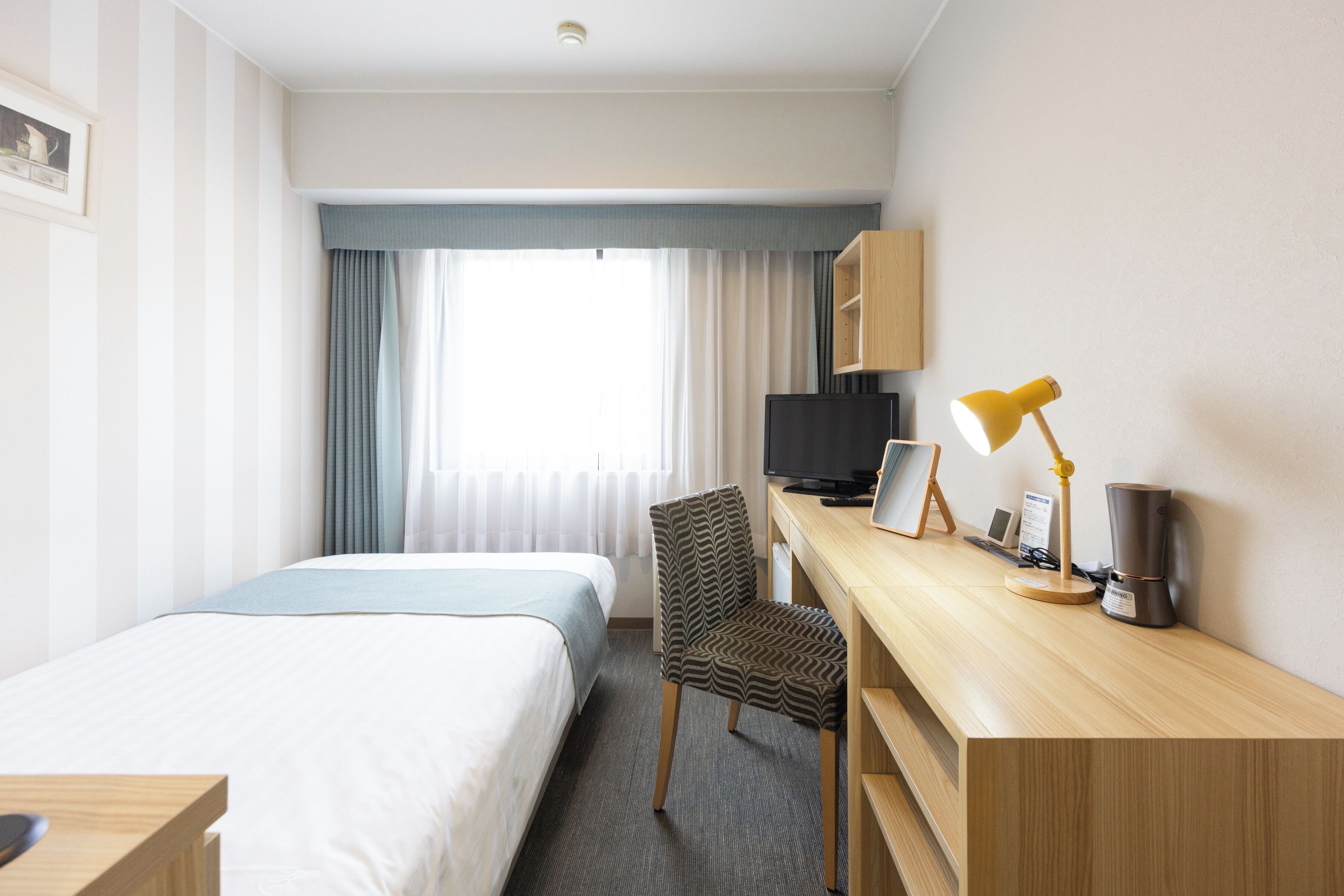 A hotel room with a bed, a desk with a computer, a chair, a television, and a coffee maker.