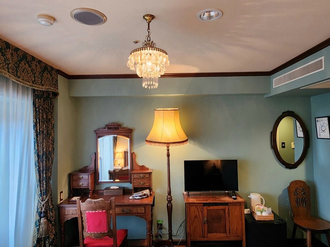 A hotel room with a desk, chair, television, lamp, and a chandelier.