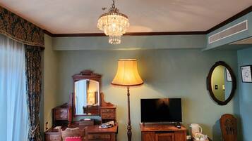 A hotel room with a desk, chair, television, lamp, and a chandelier.