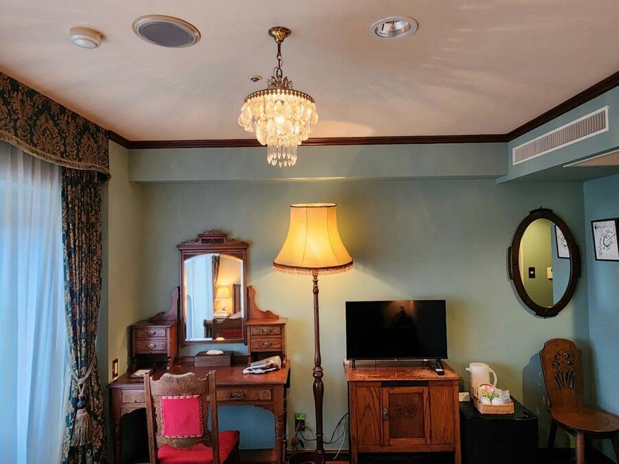 A hotel room with a desk, chair, television, lamp, and a chandelier.