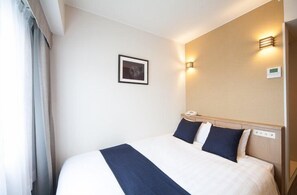 Quarto de hotel com uma cama grande, uma mesa de cabeceira com abajur, um quadro na parede e um termostato fixado na parede.
