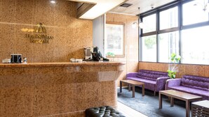 Zona de recepción de un hotel con mostrador de mármol, un sofá, una mesa y un ventanal con vistas al exterior.
