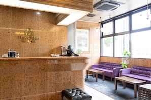 A hotel reception area with a marble counter, a sofa, a table, and a window providing a view outside.