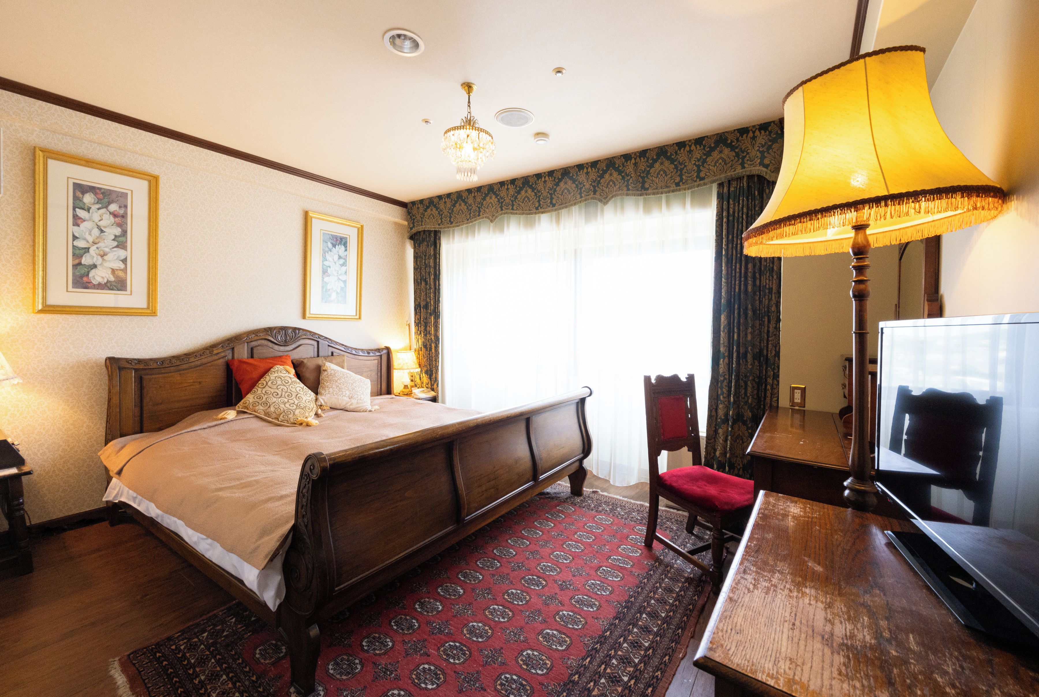 A hotel room with a bed, a desk, a chair, a lamp, a mirror, and a television.